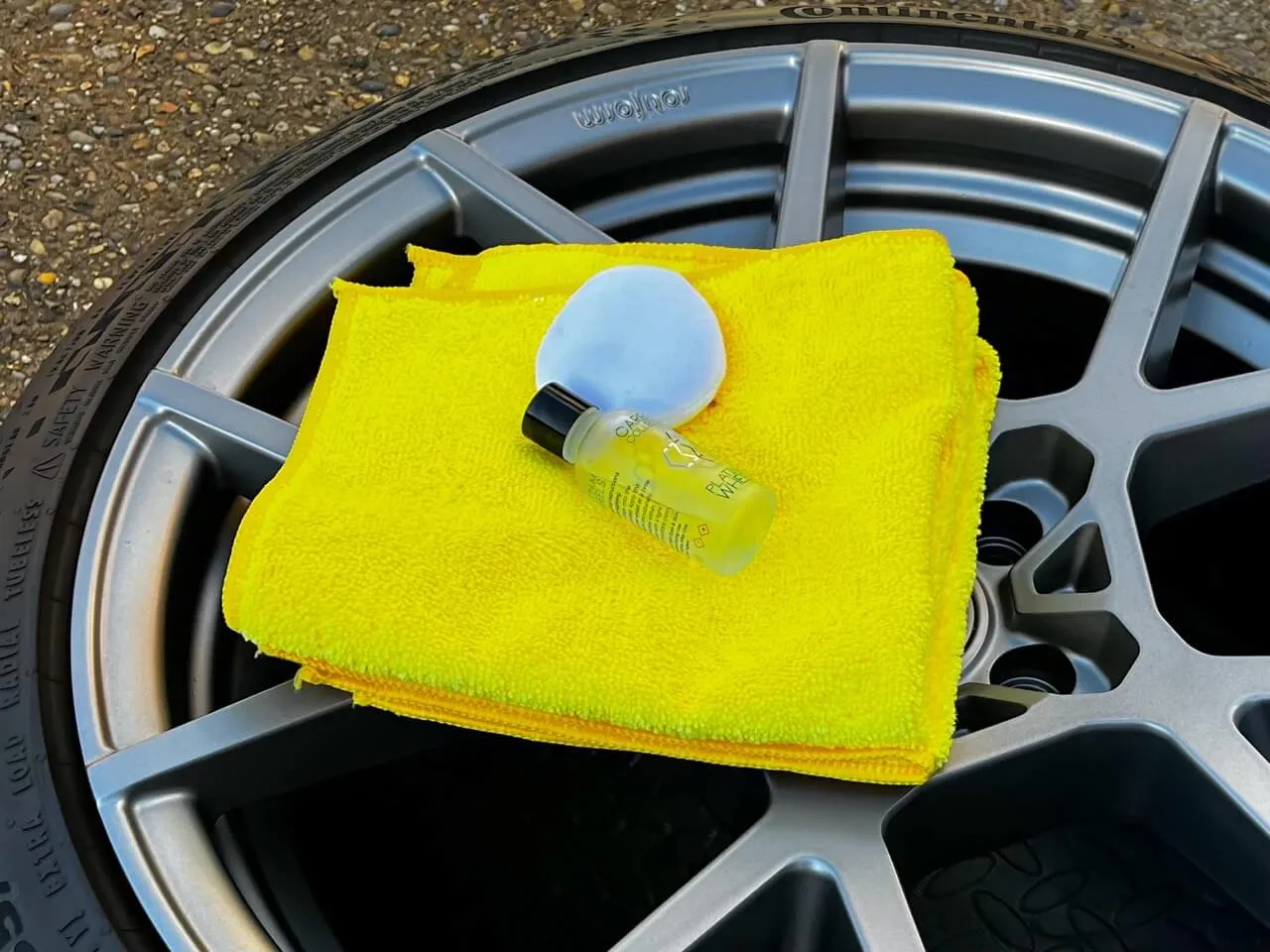 Yellow microfiber cloth with white applicator pad and ceramic coating on top of grey alloy wheel