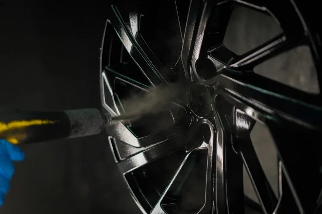 A close up of an alloy wheel being powder coated black in the spray booth
