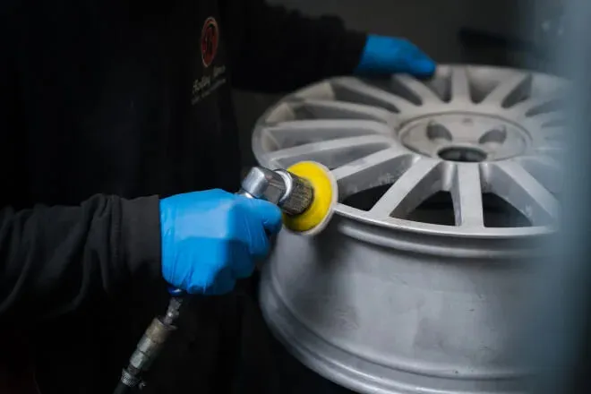 Alloy wheel being prepped for paint using a sanding wheel to achieve a smooth level finish