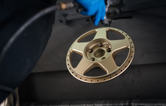 Split rim alloy hanging in the spray booth being painted in the colour gold after being repaired