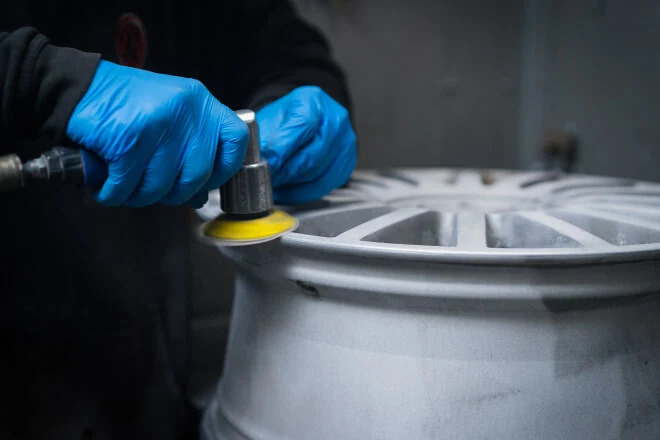Alloy wheel being prepped for paint using a sanding wheel to achieve a smooth level finish